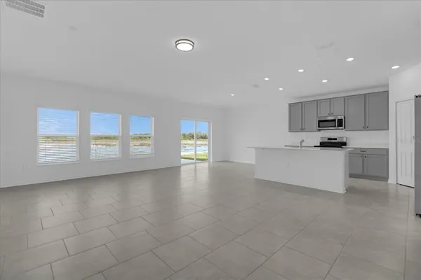 a view of an empty room with kitchen and window