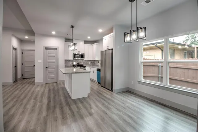 a large kitchen with stainless steel appliances kitchen island granite countertop a refrigerator a stove a sink dishwasher and white cabinets with wooden floor