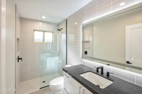 a bathroom with a granite countertop sink a toilet a mirror and shower