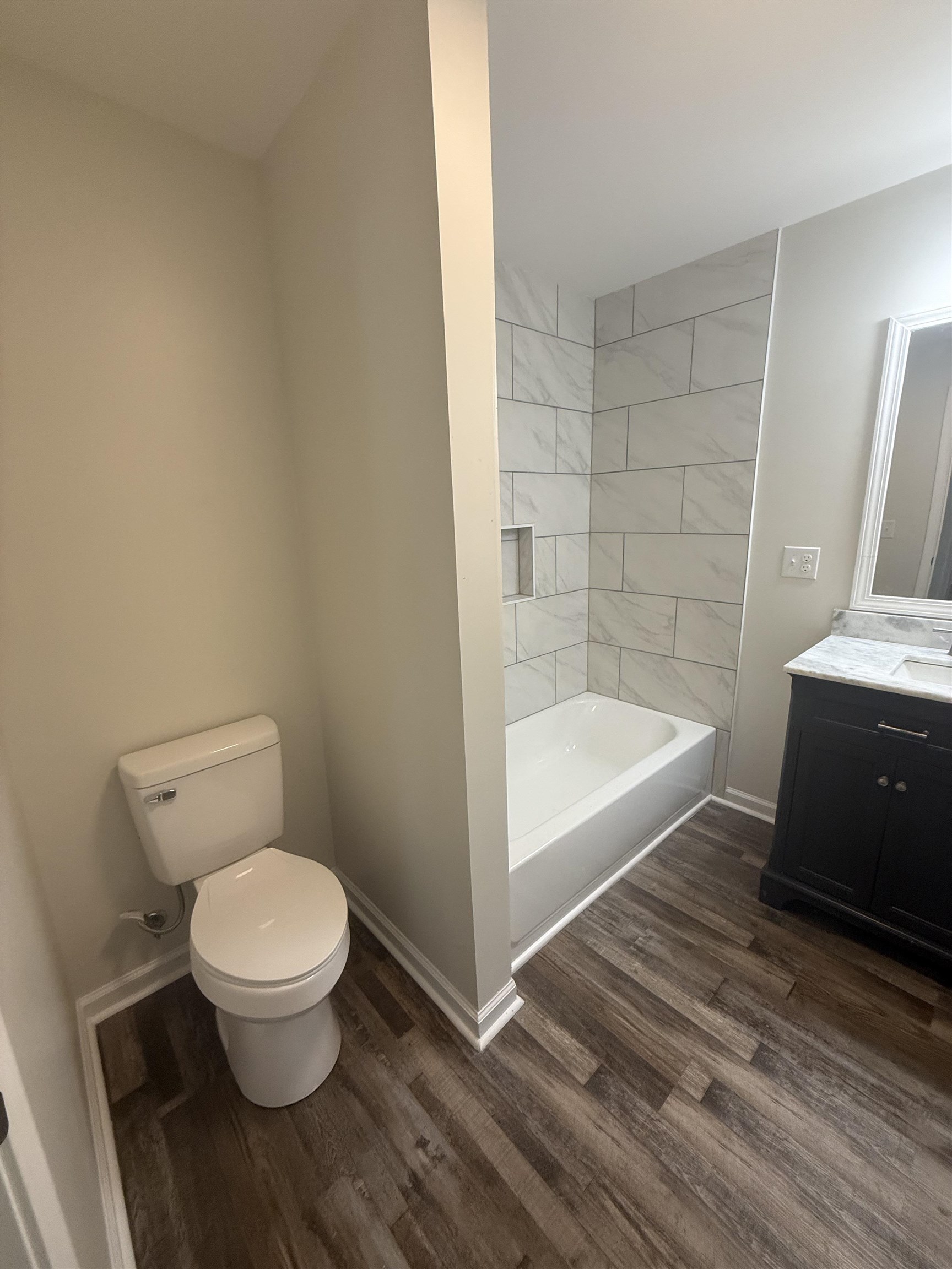 170 Leapwood Road Enville, TN 38332 - Photo 27 of 33 Bathroom featuring a full tub/shower combination with tiled surround and built-in niche, wood-finish flooring, a contemporary vanity with a stone countertop, and a white toilet