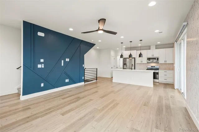 a view of an empty room and kitchen with wooden floor