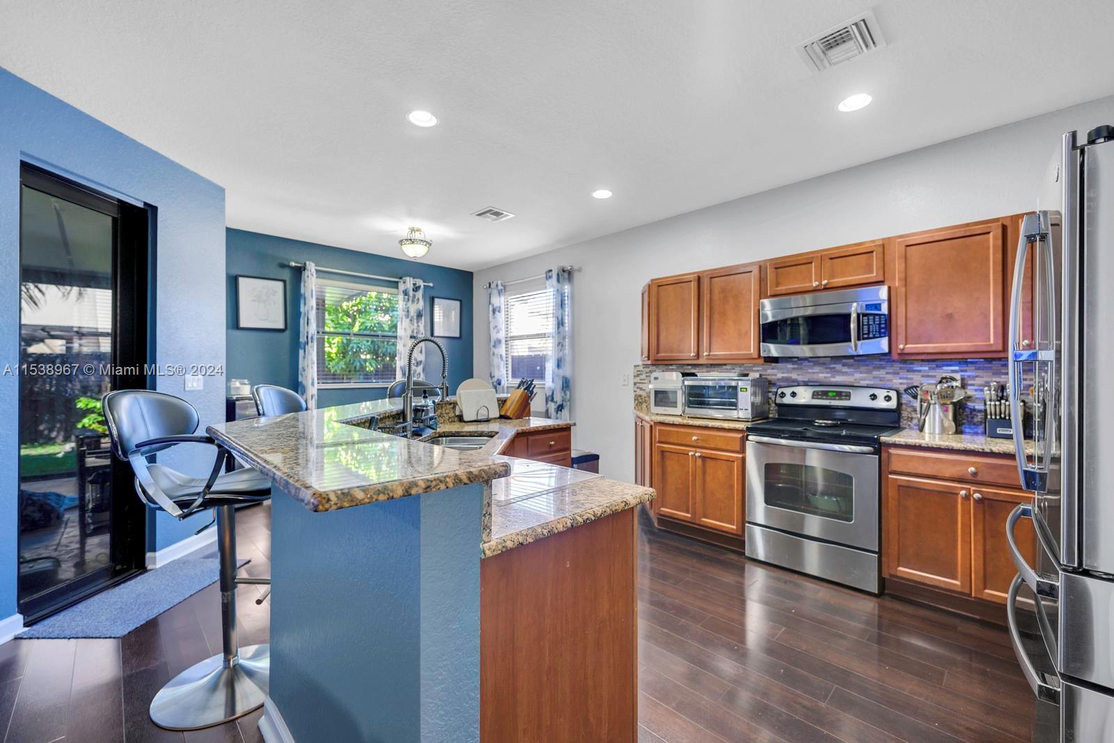 24084 Southwest 113th Path Homestead, FL 33032 - Photo 7 of 37 a kitchen with stainless steel appliances granite countertop wooden cabinets a sink a stove a dining table and chairs