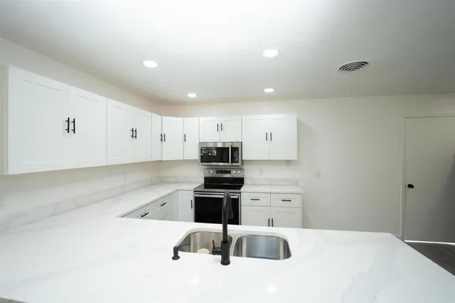 a kitchen that has a lot of white cabinets and stainless steel appliances