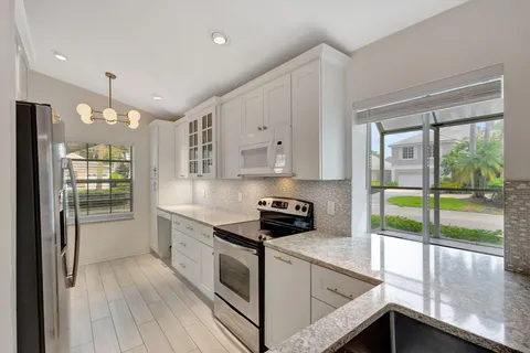 a kitchen with granite countertop a stove a sink and white cabinets with wooden floors