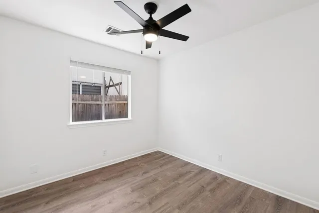 an empty room with wooden floor ceiling fan and window