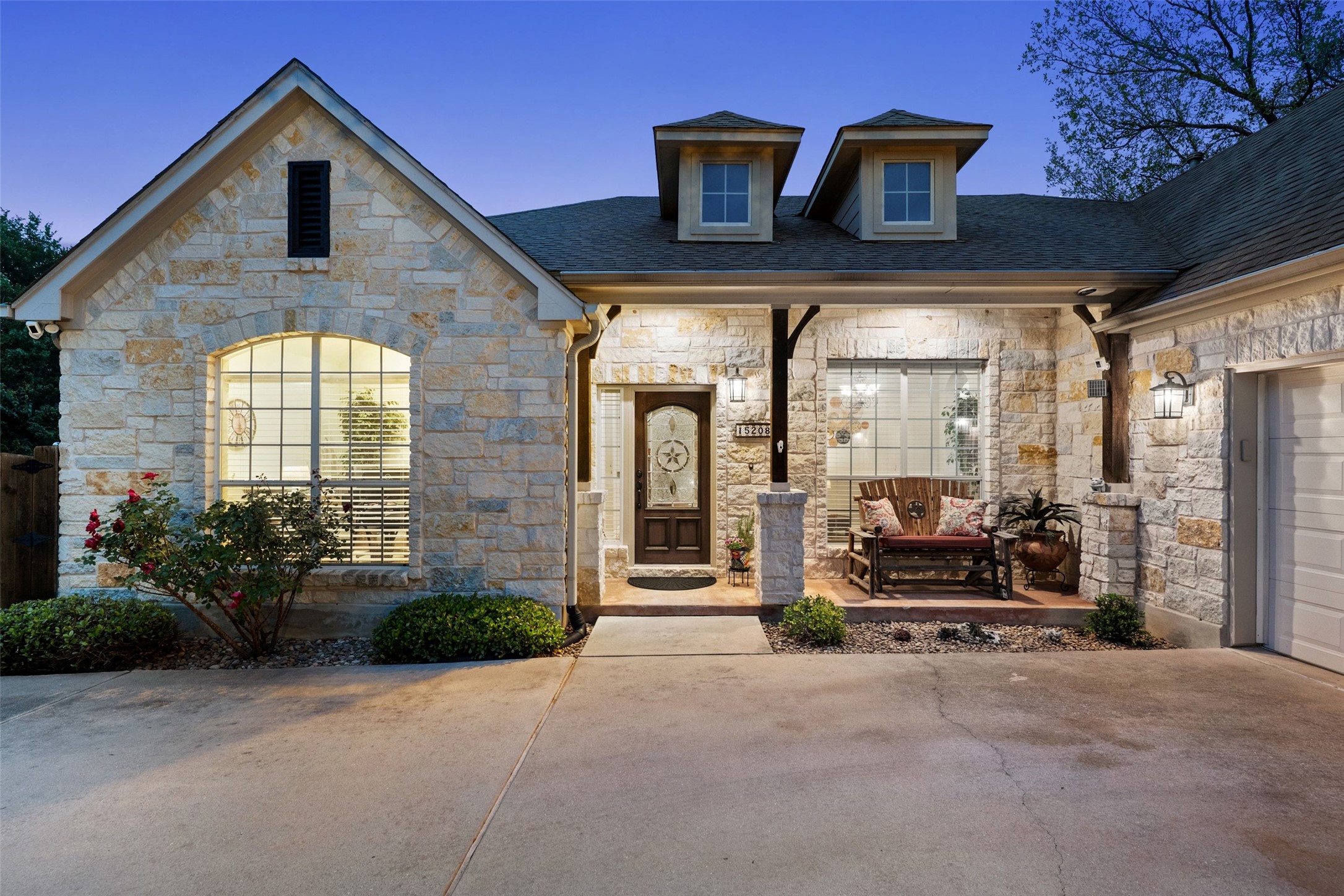 15208 Nightingale Lane Austin, TX 78734 - Photo 5 of 40 Exterior entry at dusk with stone siding, a porch, and a shingled roof
