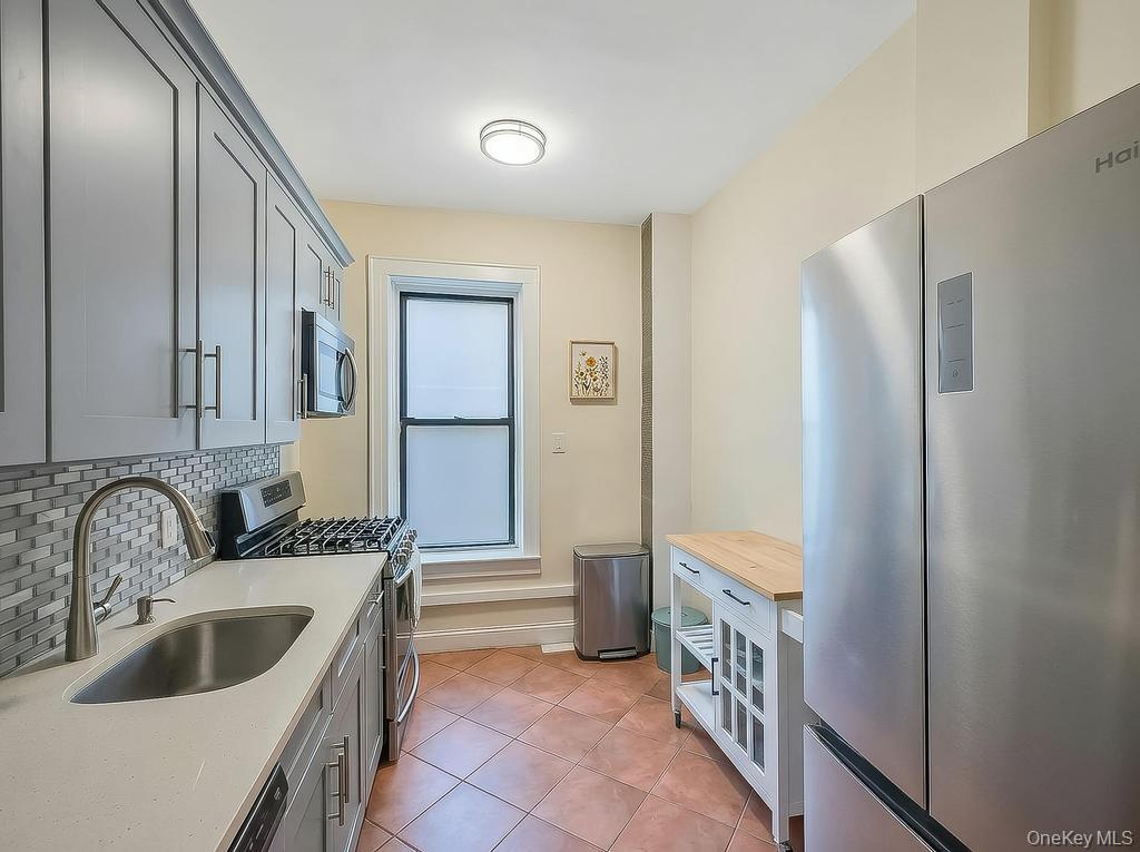83-64 Talbot Street, Unit 3A Queens, NY 11415 - Photo 4 of 15 Modern kitchen featuring stainless steel appliances, grey cabinetry, a mosaic tile backsplash, a single-basin sink with a gooseneck faucet, and terracotta-toned floor tile