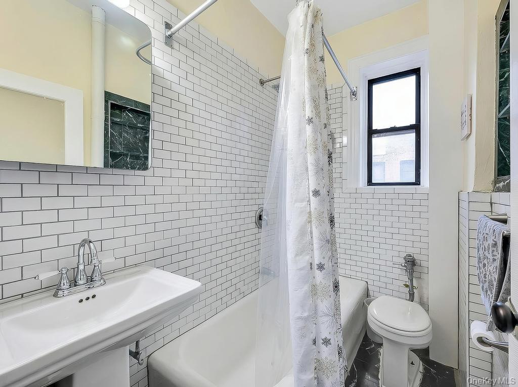 83-64 Talbot Street, Unit 3A Queens, NY 11415 - Photo 6 of 15 Bathroom featuring white subway tile walls, a pedestal sink with chrome faucet, a standard bathtub, a window with black trim, and dark stone flooring