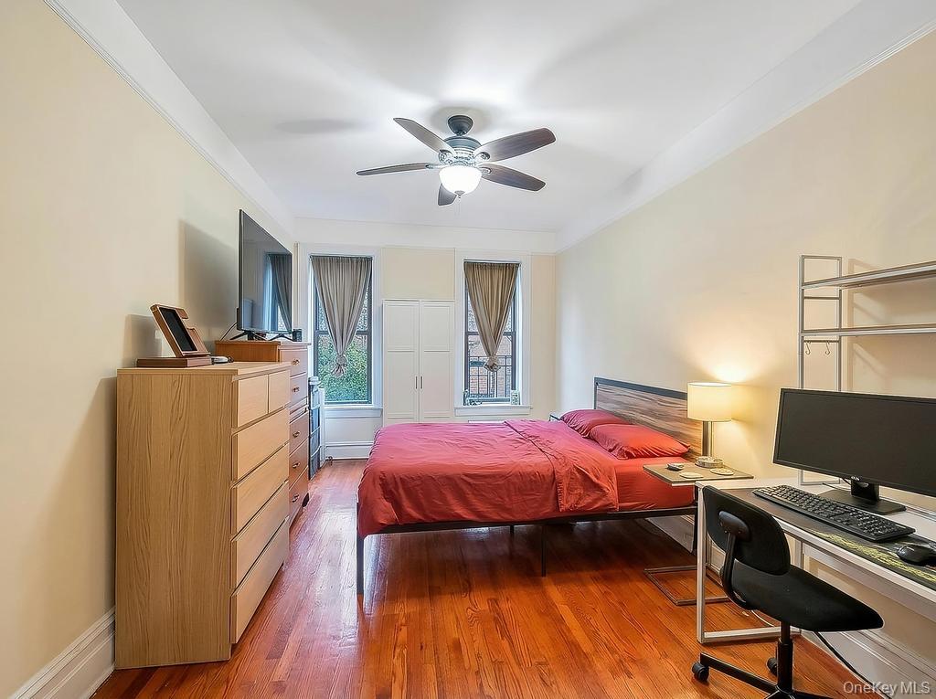83-64 Talbot Street, Unit 3A Queens, NY 11415 - Photo 8 of 15 Bedroom featuring wood-finish flooring, two windows with window treatments, a ceiling fan with integrated lighting, and crown molding