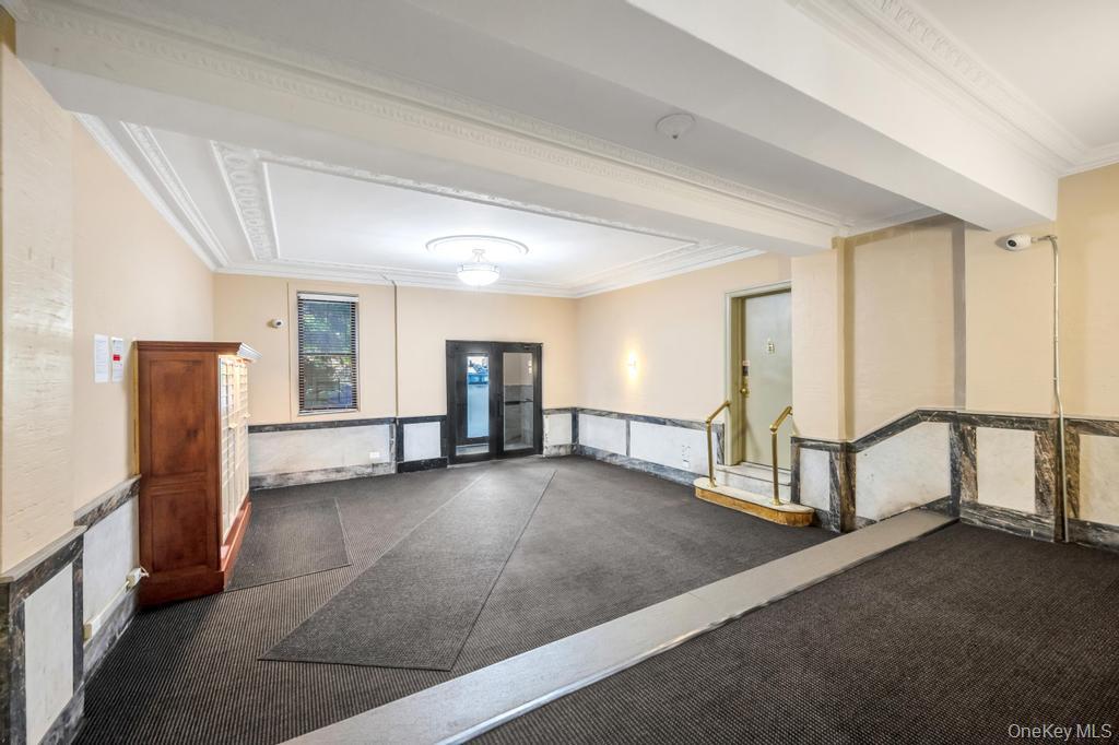 83-64 Talbot Street, Unit 3A Queens, NY 11415 - Photo 9 of 15 Building entryway featuring patterned ceiling trim, wall sconces, wall-mounted lighting, mixed-material wainscoting, and carpet flooring