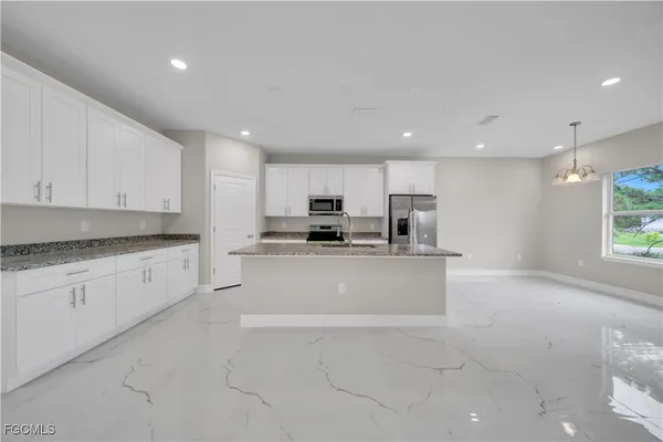 a large kitchen with stainless steel appliances granite countertop a stove a sink a refrigerator and white cabinets