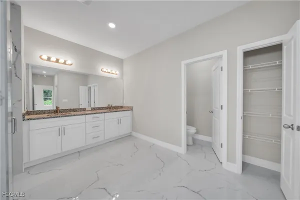 a large white bathroom with a granite countertop sink a toilet a mirror and shower