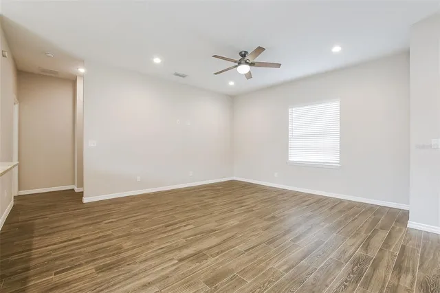 an empty room with wooden floor fan and windows