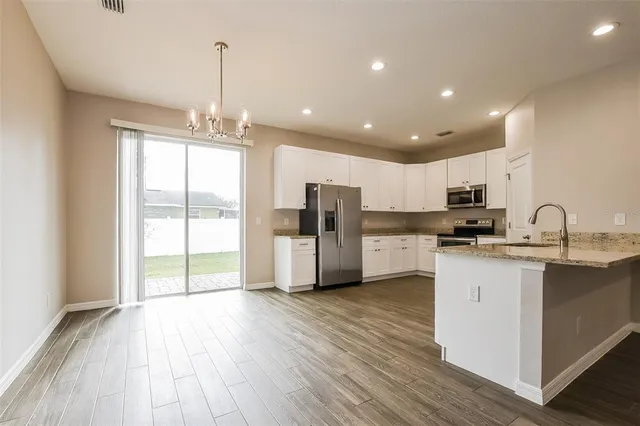 a kitchen with stainless steel appliances granite countertop a refrigerator a sink dishwasher a stove and white cabinets with wooden floor