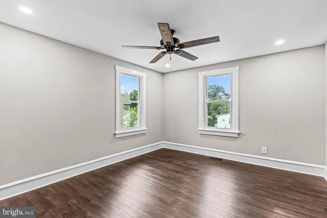 an empty room with wooden floor ceiling fan and windows
