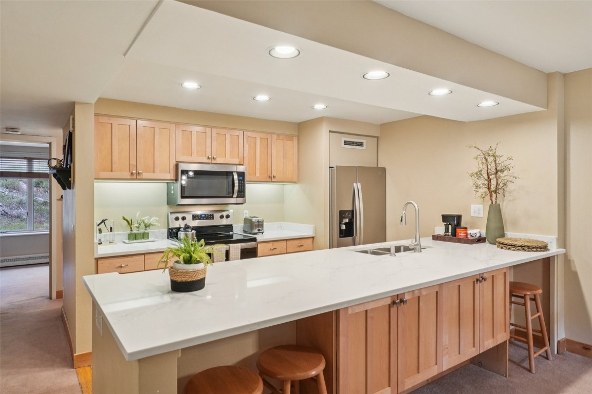Kitchen featuring a kitchen breakfast bar, light colored carpet, light brown cabinets, appliances with stainless steel finishes, and recessed lighting