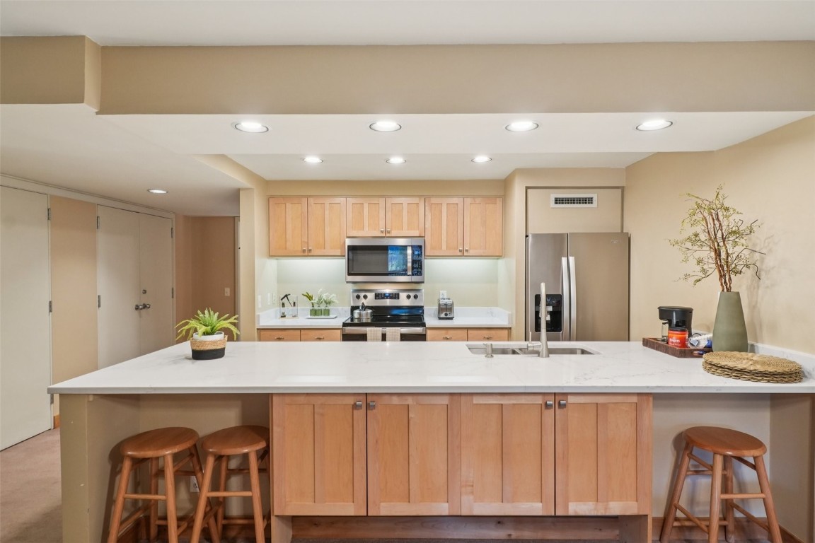 22097 Saints John Road, Unit 2506 Keystone, CO 80435 - Photo 4 of 47 Kitchen featuring light brown cabinets, a breakfast bar, appliances with stainless steel finishes, recessed lighting, and light stone countertops