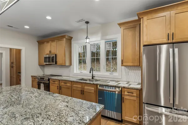 a kitchen with stainless steel appliances granite countertop a refrigerator a sink dishwasher a stove with wooden cabinets and floor