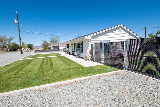 340 West 100 N Street Beaver, UT 84713 - Photo 7 of 37 White horizontal siding exterior with a pitched roof, front lawn with defined edges, gravel driveway, and a chain-link fence with privacy slats