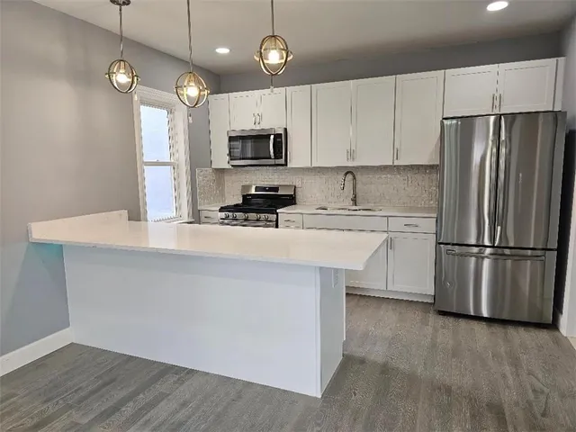 a kitchen with stainless steel appliances a refrigerator a stove a sink and white cabinets