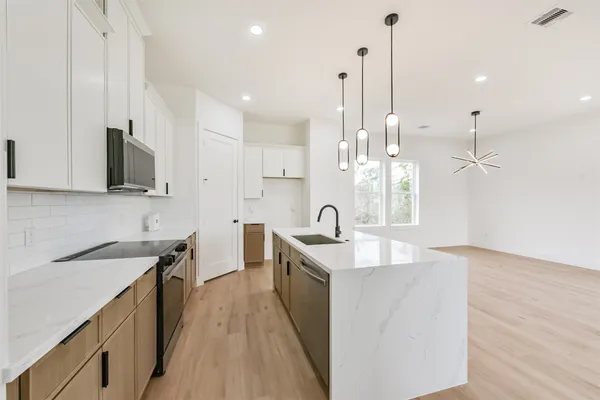 a kitchen with stainless steel appliances granite countertop a sink a stove a refrigerator and white cabinets with wooden floor