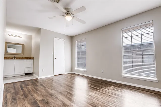 an empty room with wooden floor fan and windows