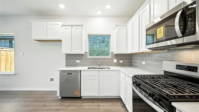 a view of an empty room with wooden floor and a kitchen