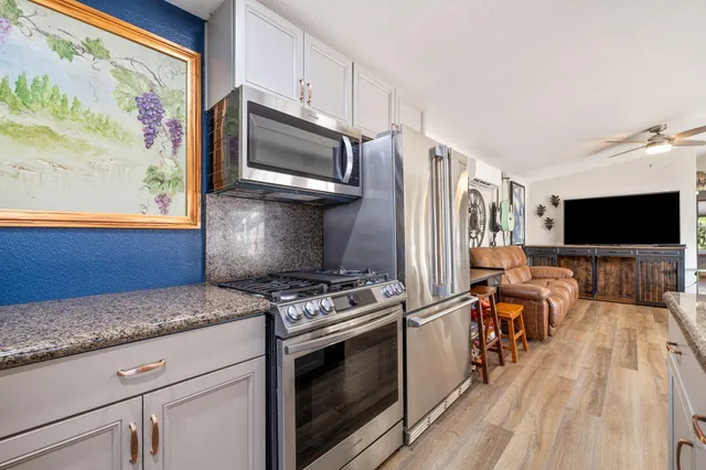 a kitchen with stainless steel appliances granite countertop a stove a microwave and a view of living room