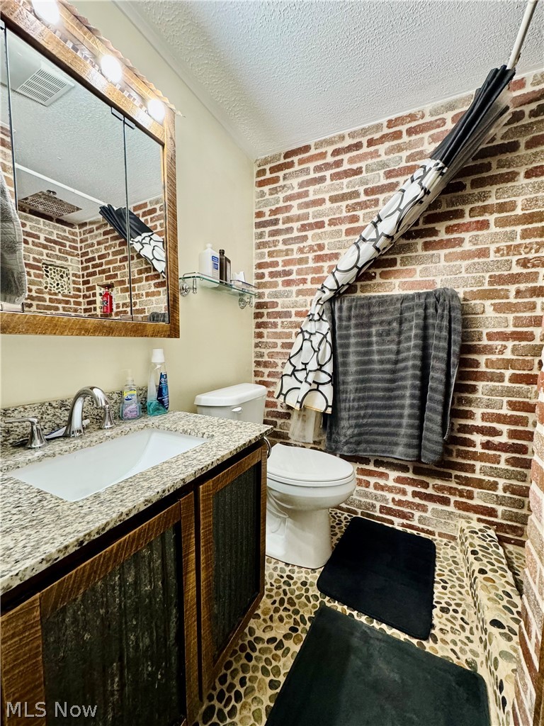 86 Cunningham Hill Road Harrisville, WV 26362 - Photo 14 of 32 Bathroom featuring a textured ceiling, toilet, vanity, tile patterned floors, and brick wall