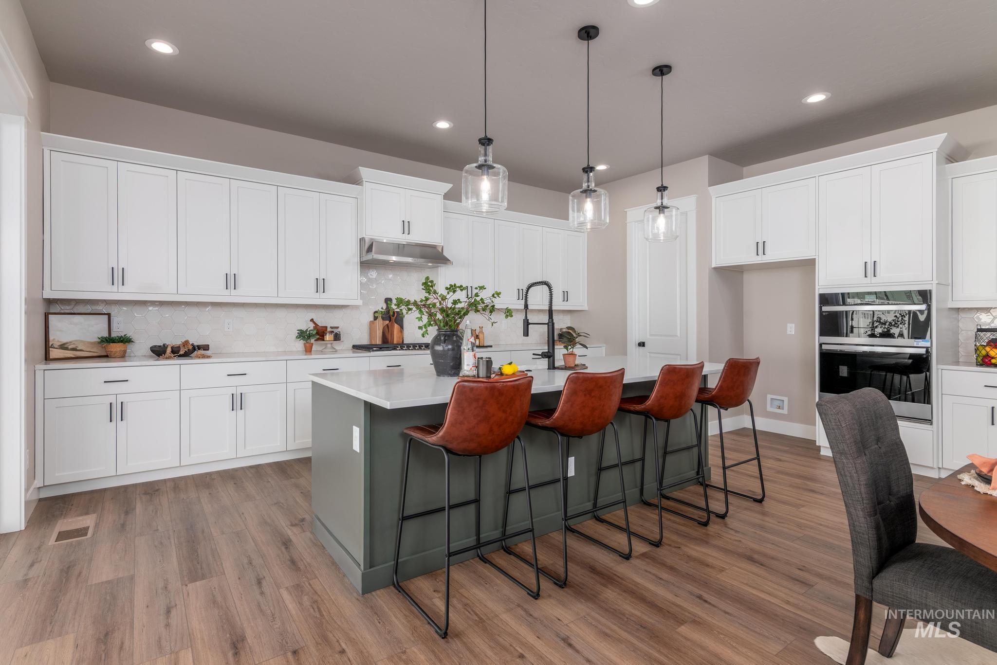 15249 Steel Cloud Avenue Caldwell, ID 83607 - Photo 11 of 46 Kitchen featuring backsplash, an island with sink, white cabinets, decorative light fixtures, and a kitchen bar