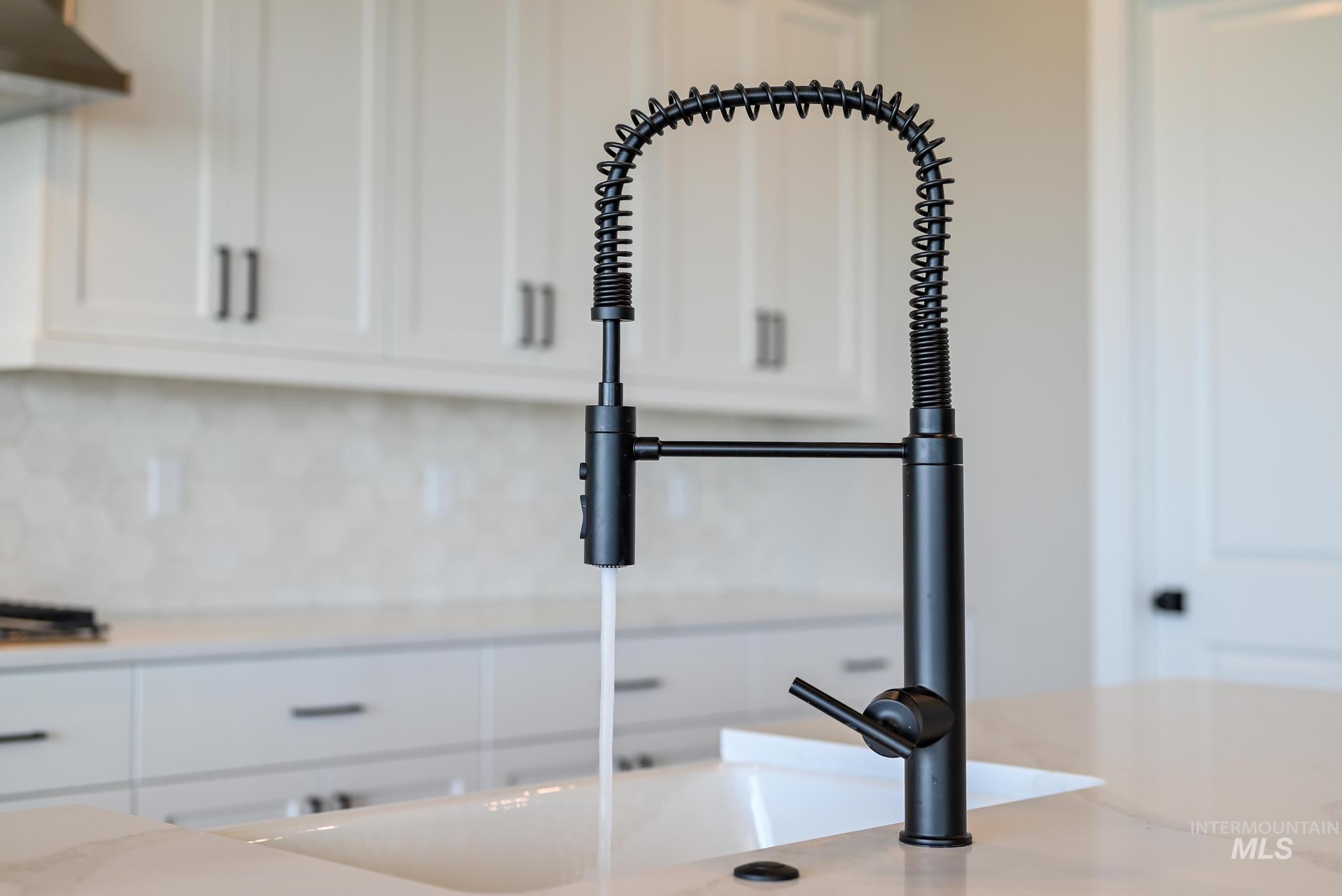 15249 Steel Cloud Avenue Caldwell, ID 83607 - Photo 18 of 46 Kitchen view of white cabinetry, light stone countertops, ventilation hood, and backsplash