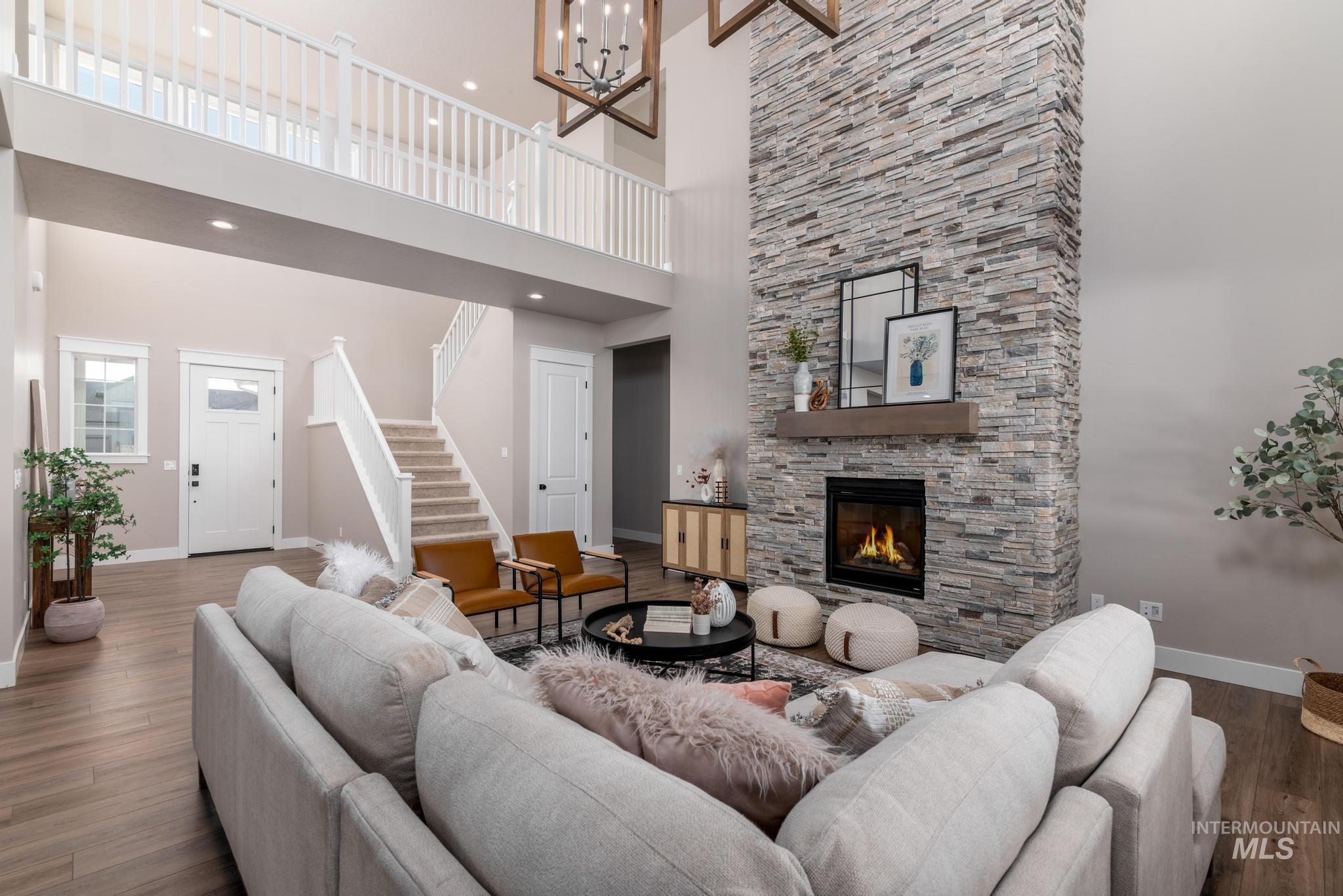 15249 Steel Cloud Avenue Caldwell, ID 83607 - Photo 6 of 46 Living area featuring dark wood finished floors, a stone fireplace, stairs, a high ceiling, and a chandelier