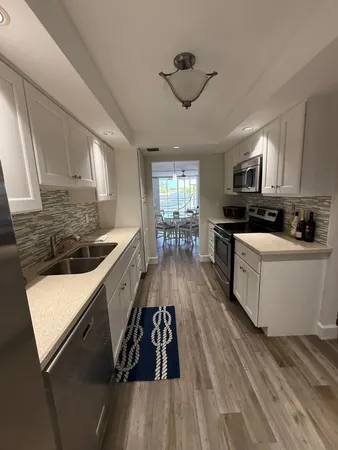 a kitchen with granite countertop a stove top oven a sink dishwasher and white cabinets with wooden floor