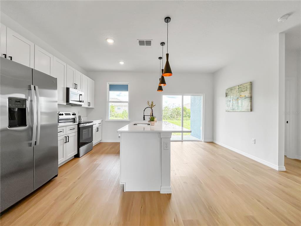 16212 Southwest 48th Circle Ocala, FL 34473 - Photo 7 of 17 a kitchen with a refrigerator a stove top oven a sink dishwasher and white cabinets with wooden floor