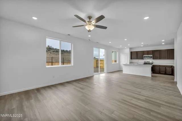 a view of an empty room with wooden floor and a kitchen