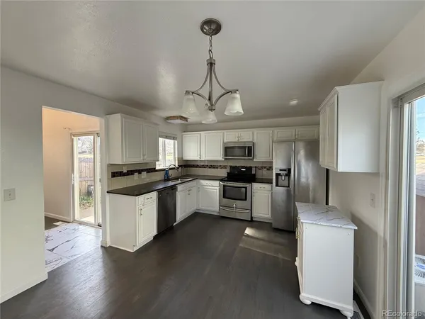 a kitchen with stainless steel appliances granite countertop a refrigerator a stove a sink dishwasher a refrigerator and white cabinets with wooden floor