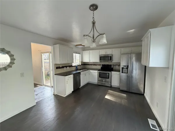 a kitchen with stainless steel appliances granite countertop a refrigerator a sink dishwasher a stove and white cabinets with wooden floor