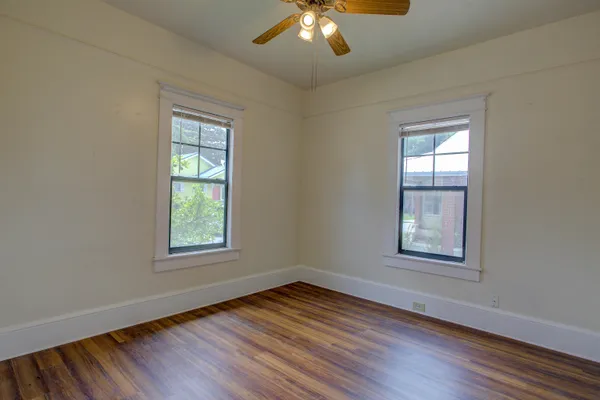 an empty room with wooden floor chandelier and windows