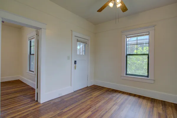an empty room with wooden floor chandelier fan and windows