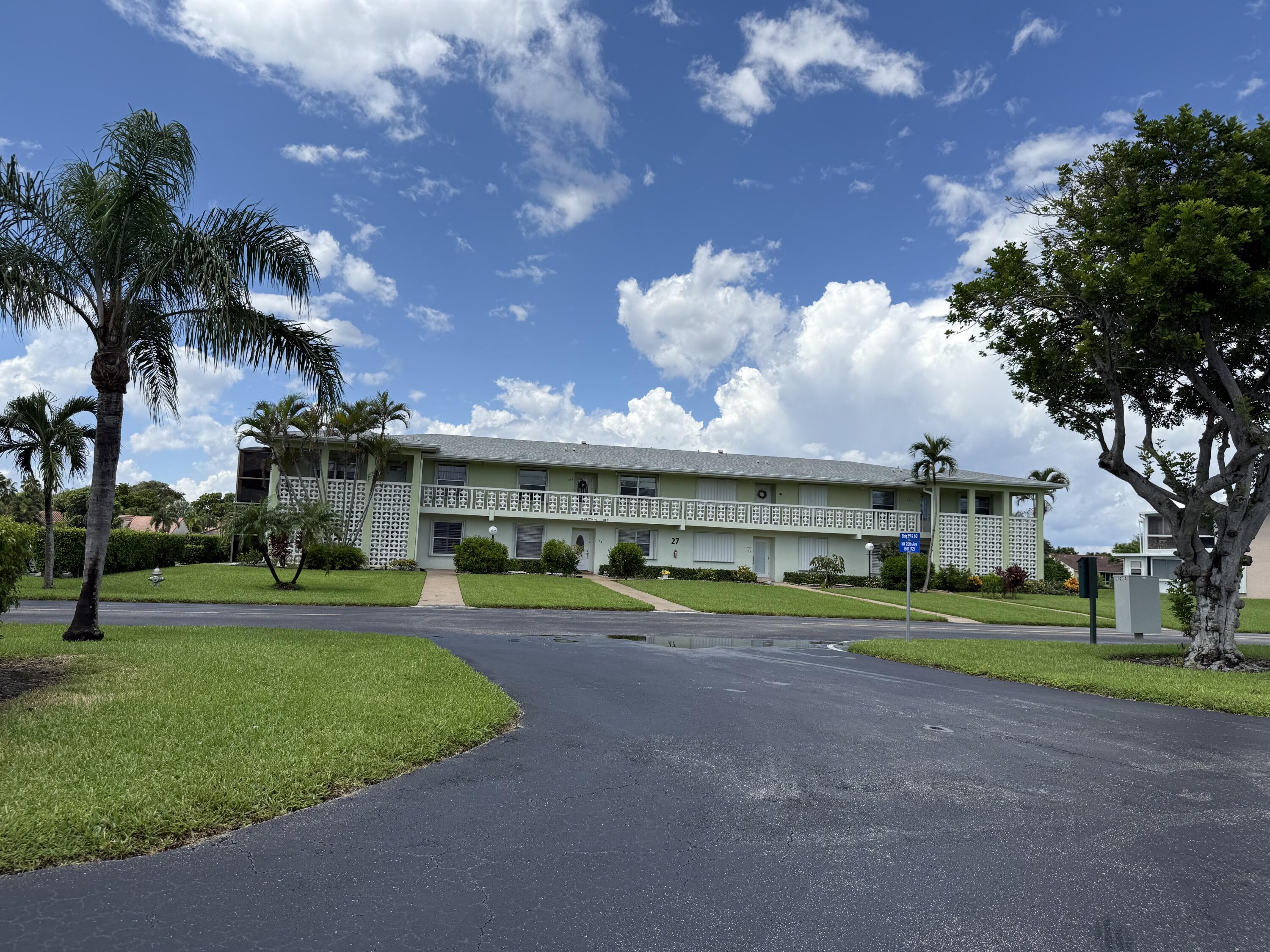 1720 Northwest 20th Avenue, Unit 204 Delray Beach, FL 33445 - Photo 2 of 30 a front view of a house with a yard and potted plants and large trees