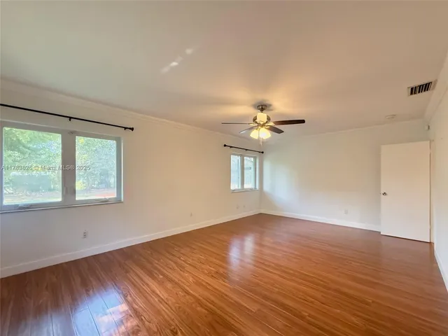 an empty room with wooden floor chandelier fan and windows