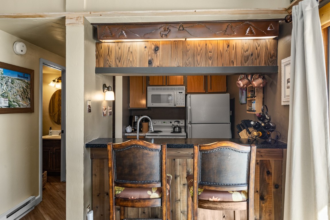 1945 Cornice Road, Unit 101D Steamboat Springs, CO 80487 - Photo 11 of 33 Kitchen with dark countertops, baseboard heating, a peninsula, brown cabinetry, and white appliances