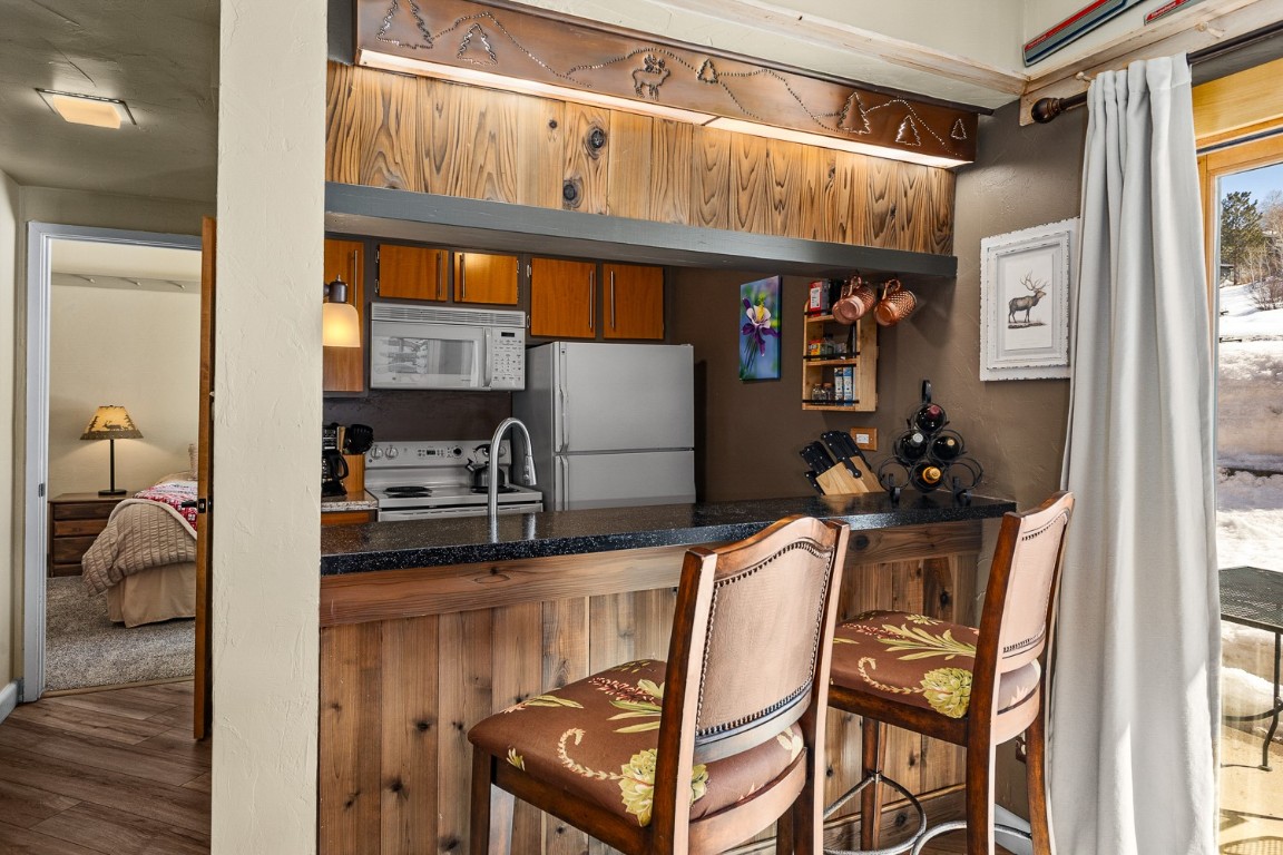 1945 Cornice Road, Unit 101D Steamboat Springs, CO 80487 - Photo 12 of 33 Kitchen with brown cabinetry, white appliances, a kitchen bar, and wood finished floors