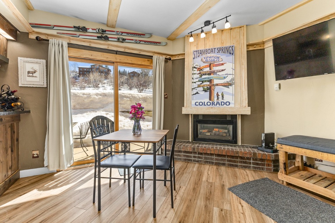 1945 Cornice Road, Unit 101D Steamboat Springs, CO 80487 - Photo 4 of 33 Dining area with track lighting, a large fireplace, baseboards, lofted ceiling with beams, and wood finished floors