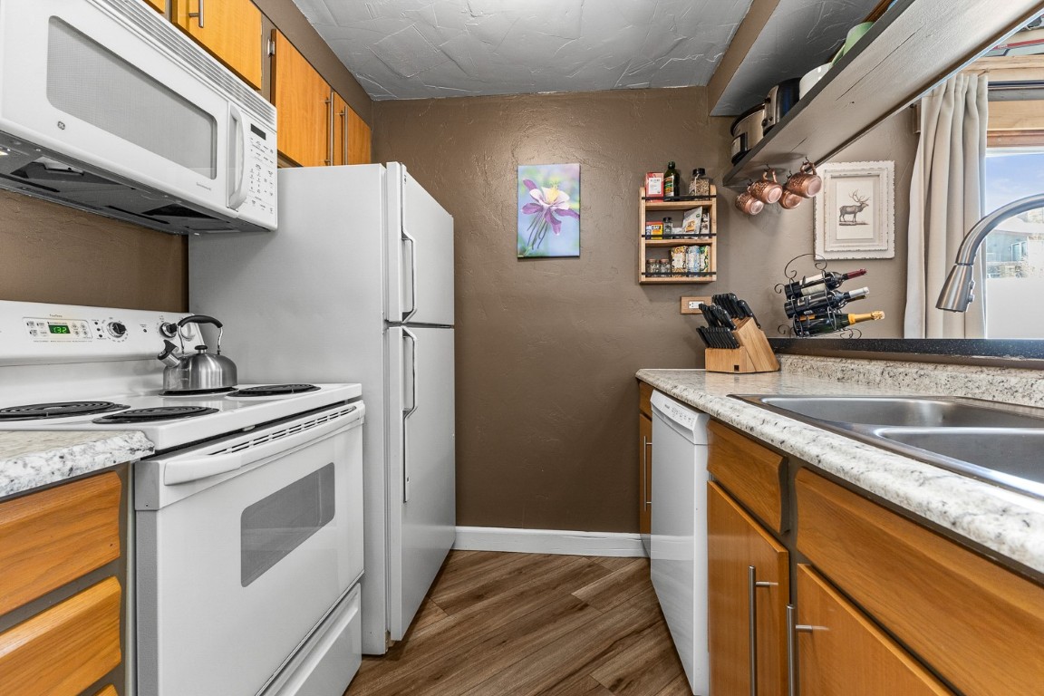1945 Cornice Road, Unit 101D Steamboat Springs, CO 80487 - Photo 7 of 33 Kitchen featuring a sink, dark LVT floors, white appliances, brown cabinetry, and baseboards