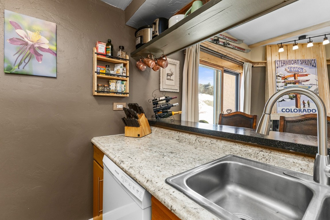 1945 Cornice Road, Unit 101D Steamboat Springs, CO 80487 - Photo 8 of 33 Kitchen with lofted ceiling, a textured wall, light stone counters, white dishwasher, and a sink