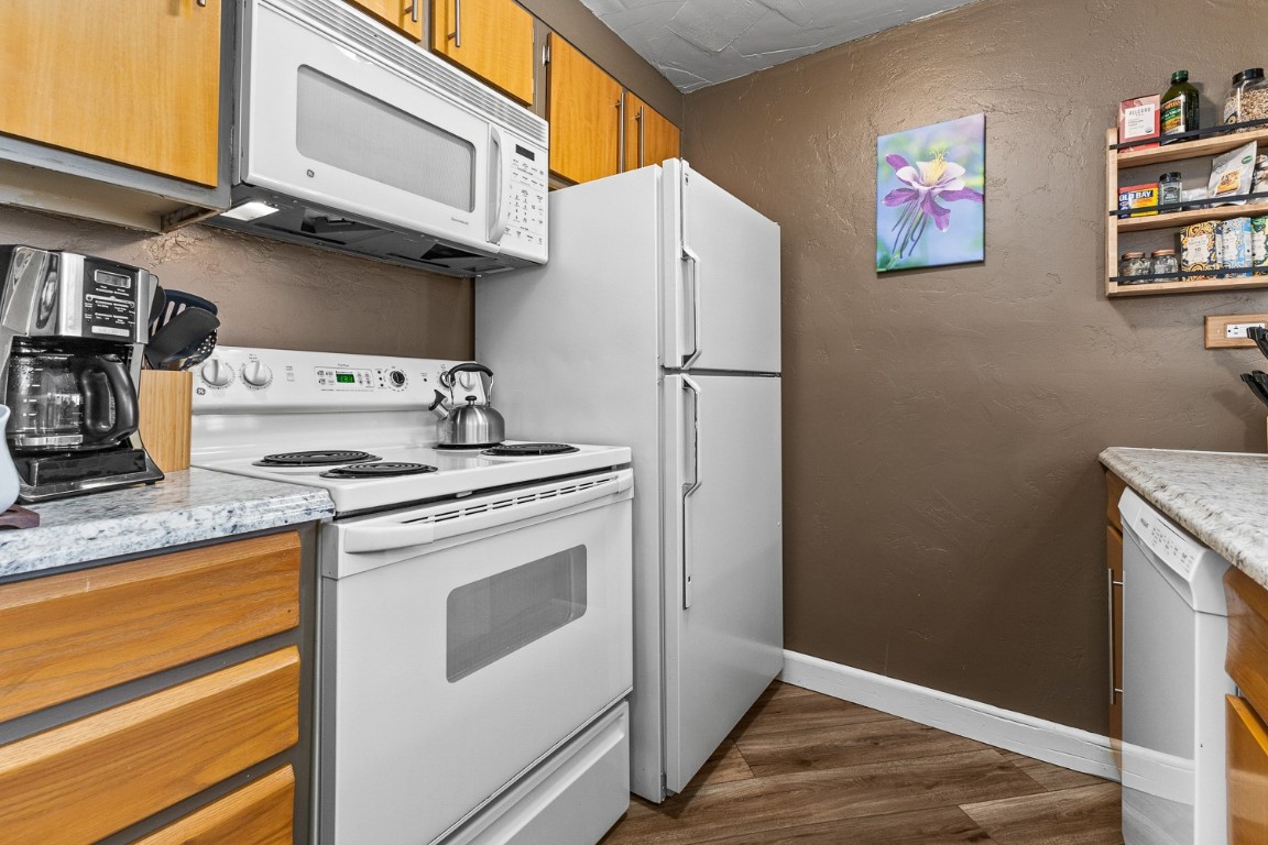 1945 Cornice Road, Unit 101D Steamboat Springs, CO 80487 - Photo 10 of 33 Kitchen featuring brown cabinetry, baseboards, a textured wall, dark wood-style floors, and white appliances
