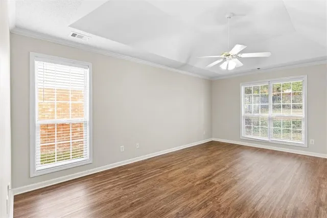 an empty room with wooden floor chandelier fan and windows