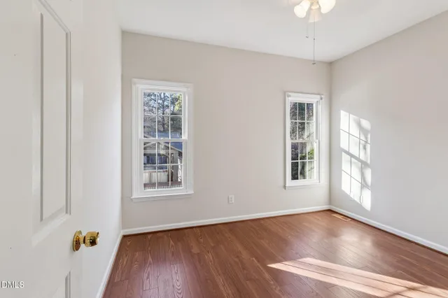 an empty room with wooden floor chandelier fan and windows