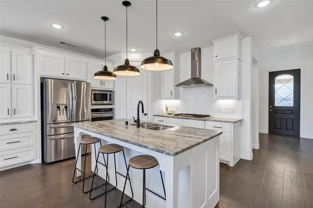 a kitchen with stainless steel appliances granite countertop a sink a stove a refrigerator and a wooden floor